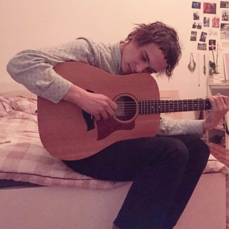 Frank Dillane is playing his guitar at his room.